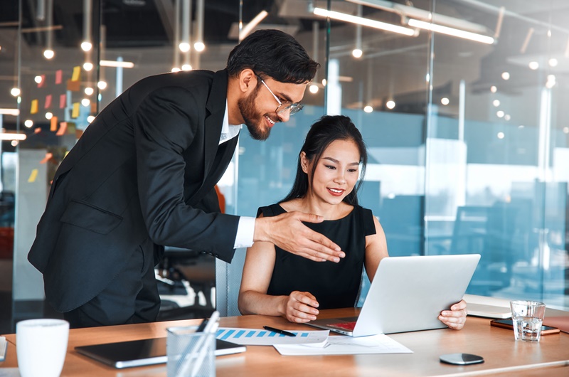 People working in a coworking space. Two business employees discussing upcoming strategy and plans while sitting at a laptop in a modern office.